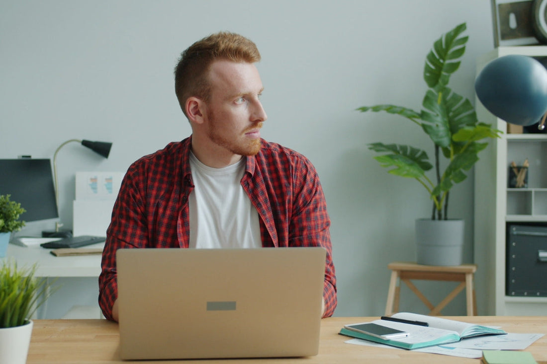 Online fundraising for nonprofits - Young man in a casual office setting working on a laptop, looking to the side.